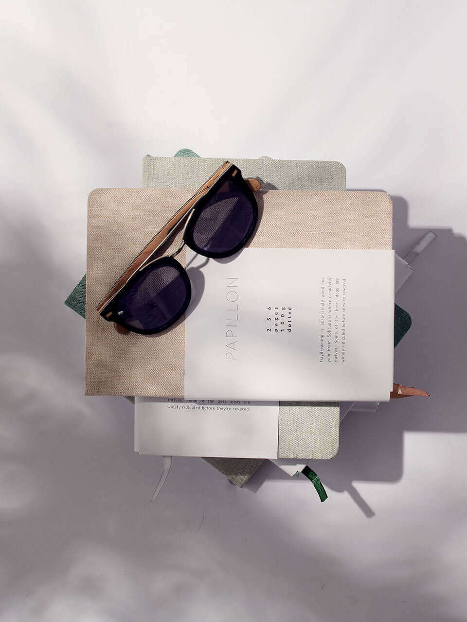 A pair of sunglasses rests atop a notebook on a table, suggesting a leisurely reading experience outdoors.