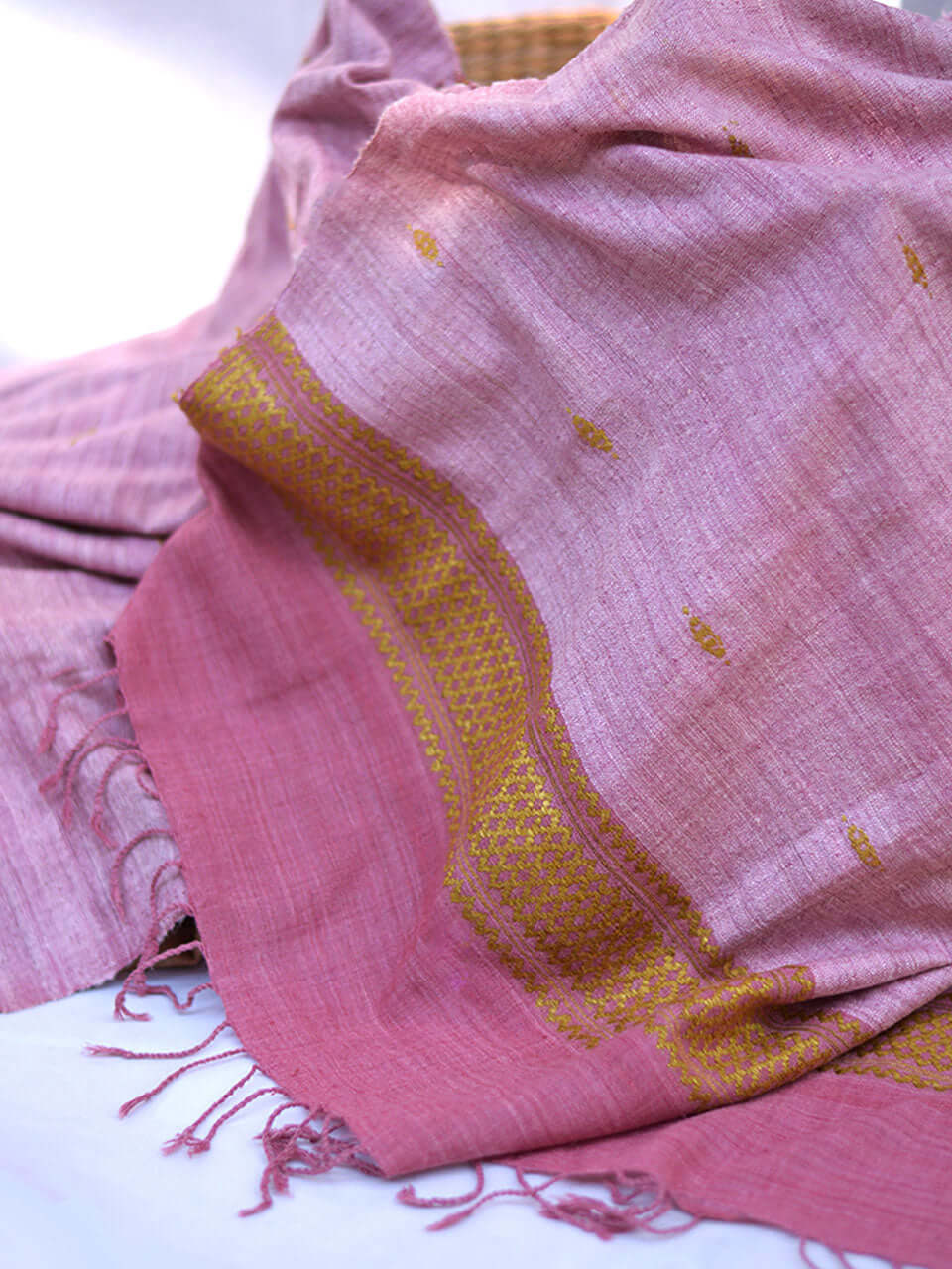 A pink scarf with intricate gold embroidery resting on a clean white surface, showcasing texture and color contrast.