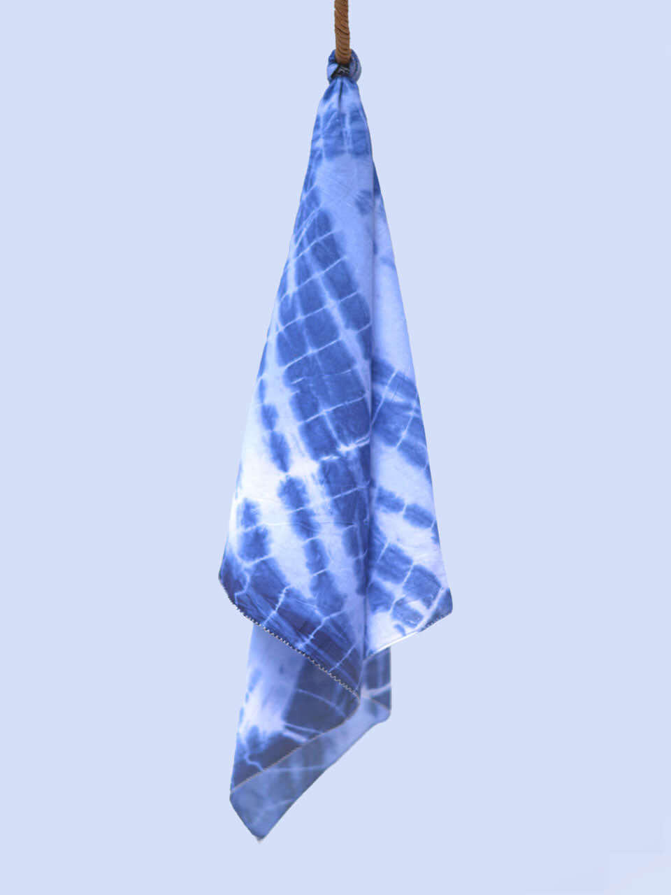 A vibrant tie-dye scarf elegantly draped against a clean white wall, showcasing its colorful patterns.