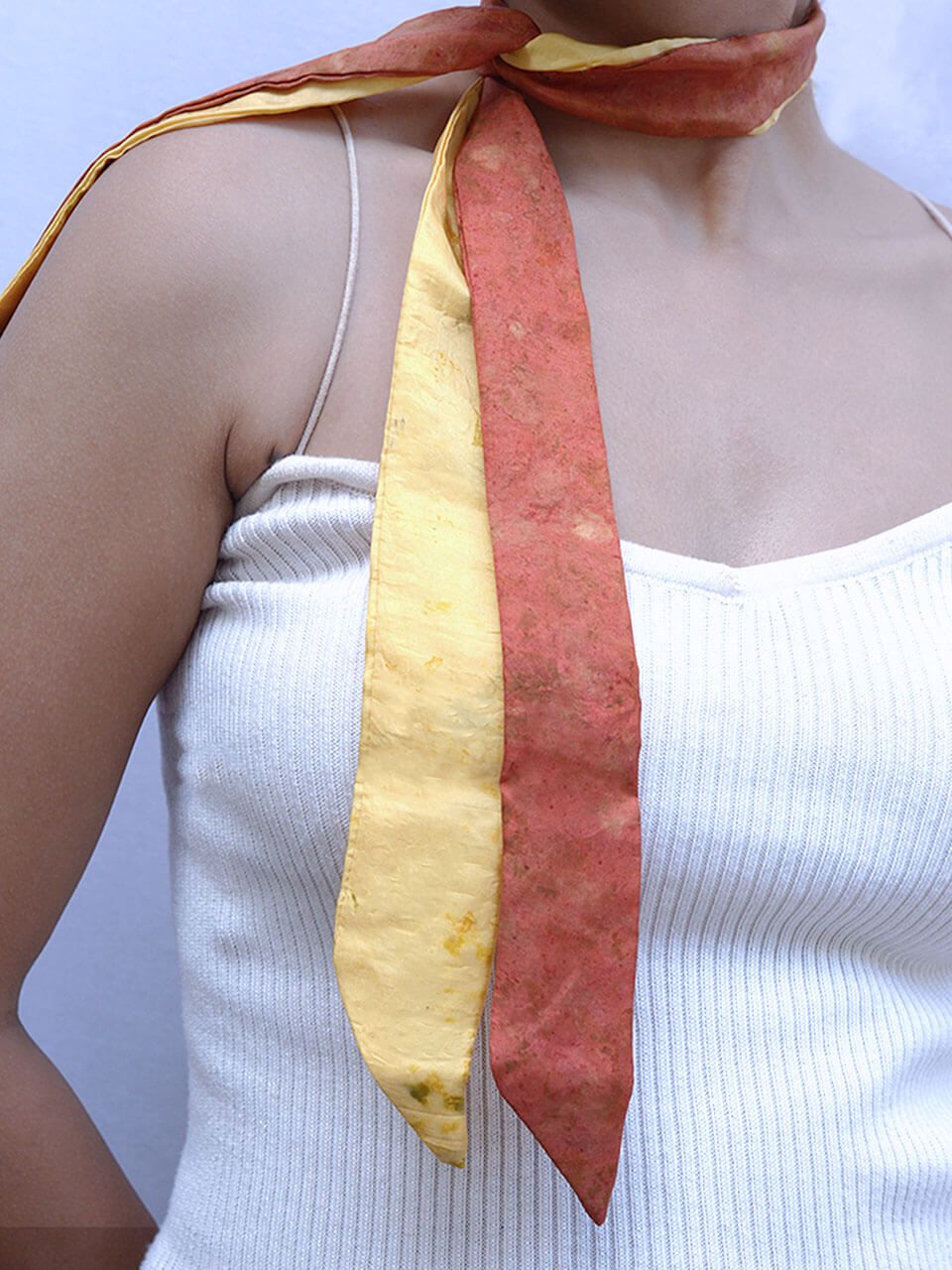 A woman in a white tank top adorned with a vibrant yellow and red scarf