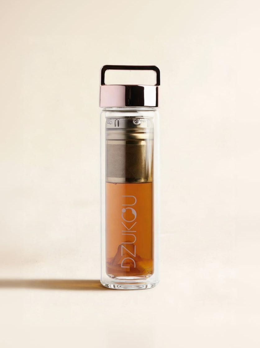 Clear glass bottle with black lid and pink top, containing a brown liquid, on a beige background.