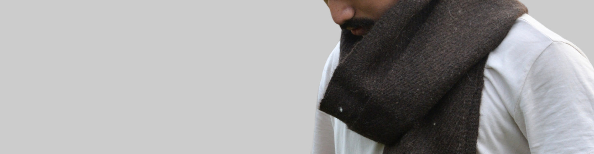 Man wearing a dark brown scarf over a light-colored shirt against a light blue background