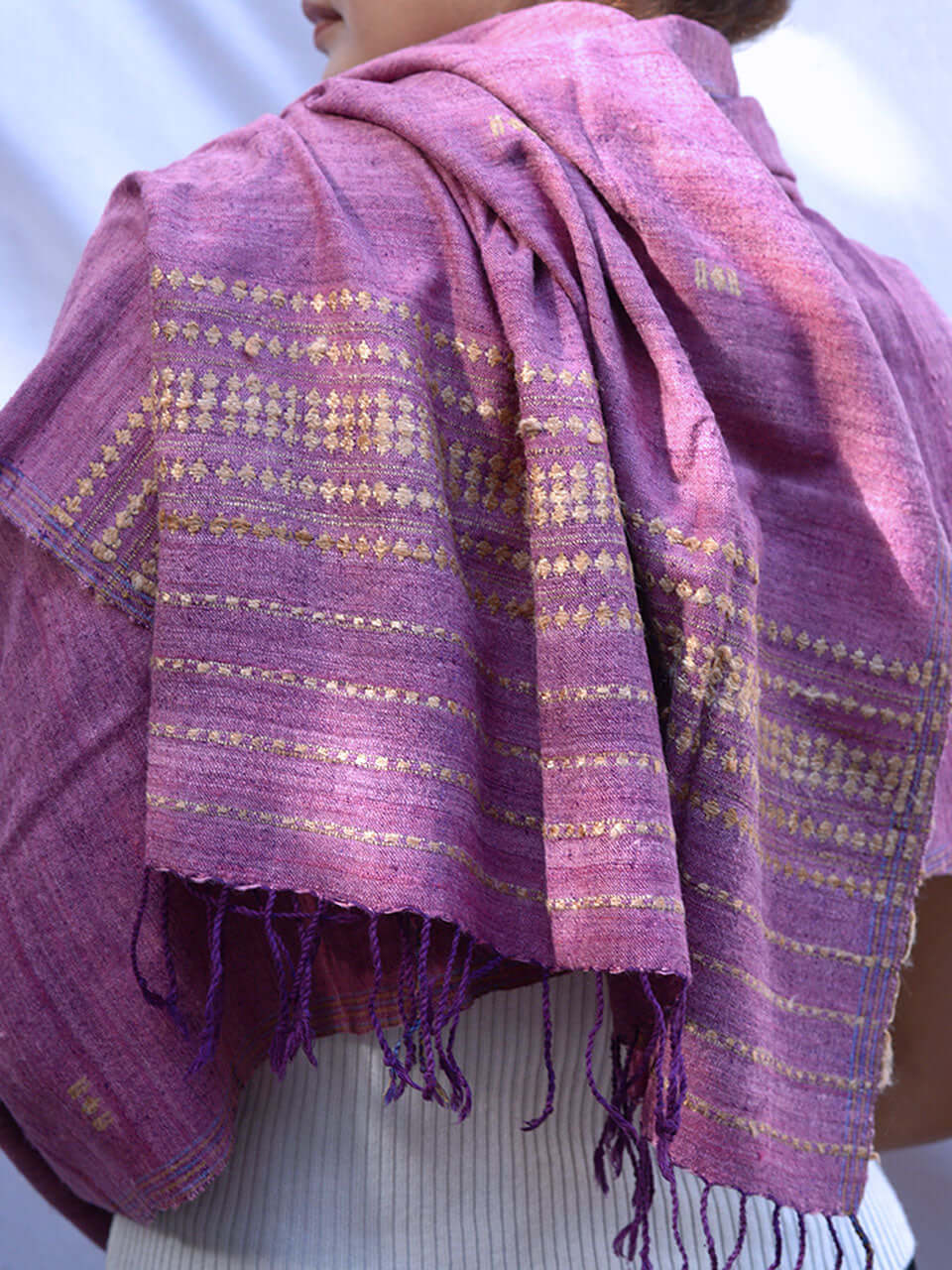 A woman elegantly draped in a purple scarf adorned with striking gold and purple stripes