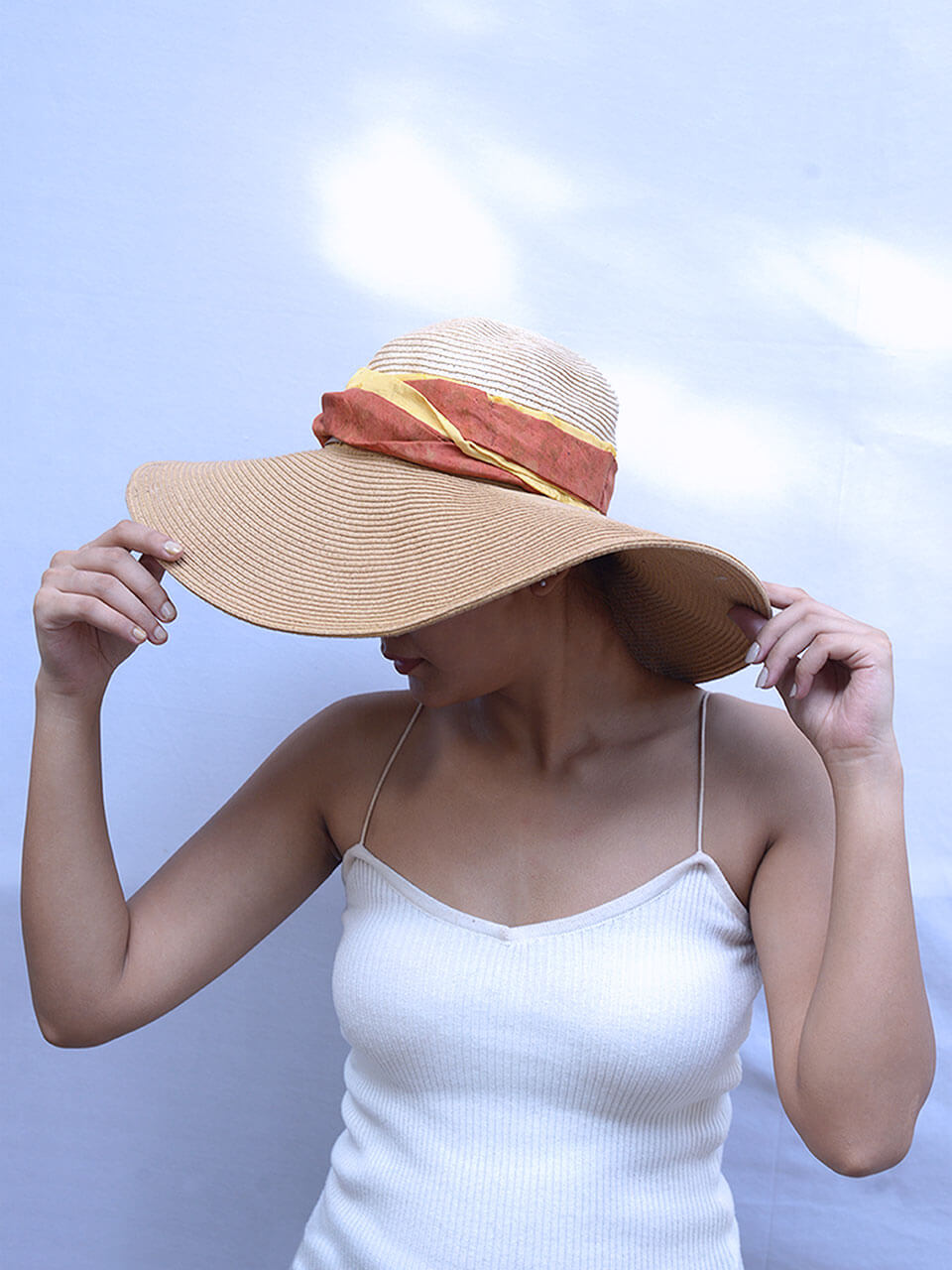 A woman in a hat and tank top stands confidently, showcasing a casual yet stylish summer look