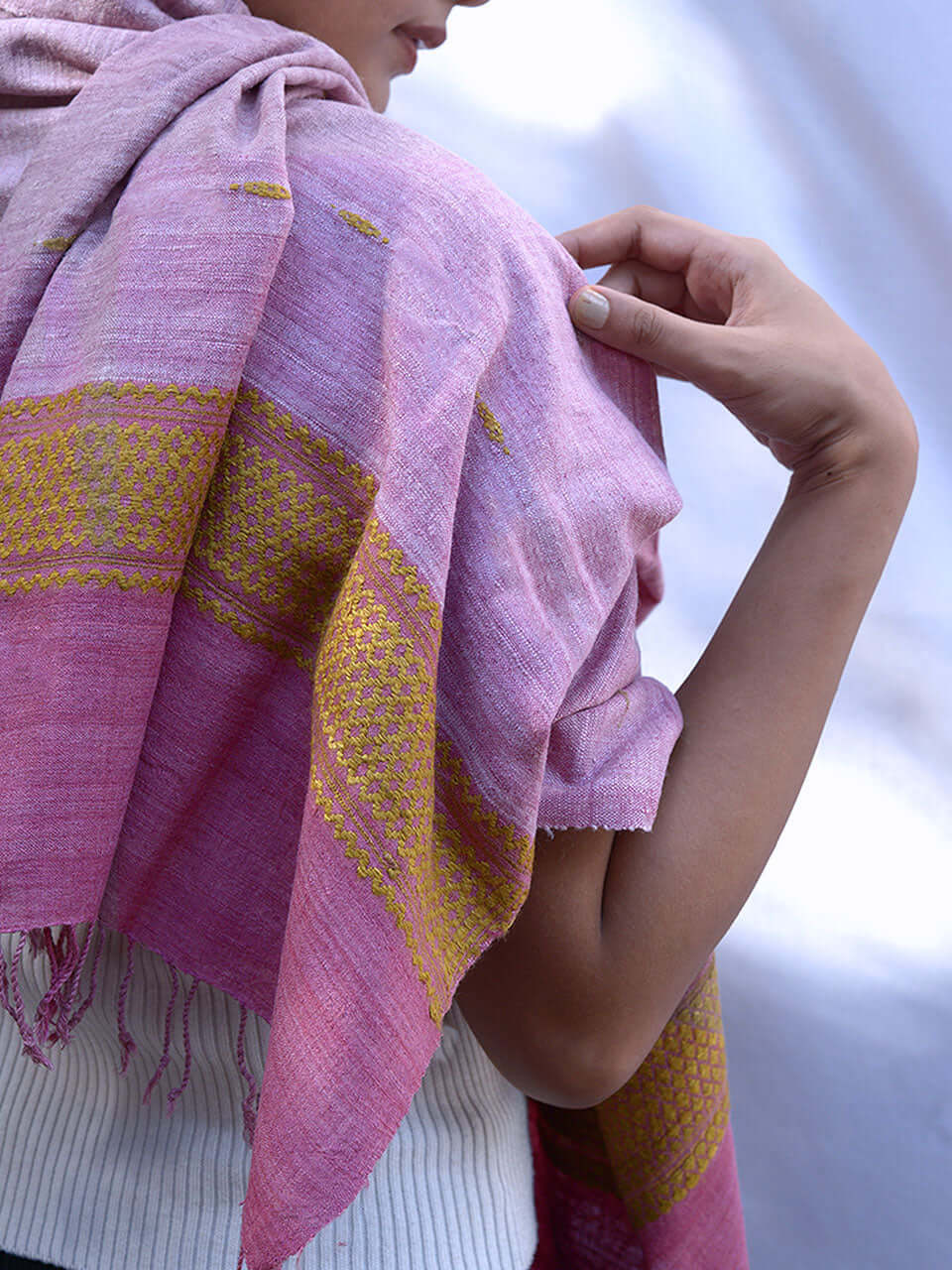 A woman elegantly draped in a pink scarf adorned with intricate gold embroidery.