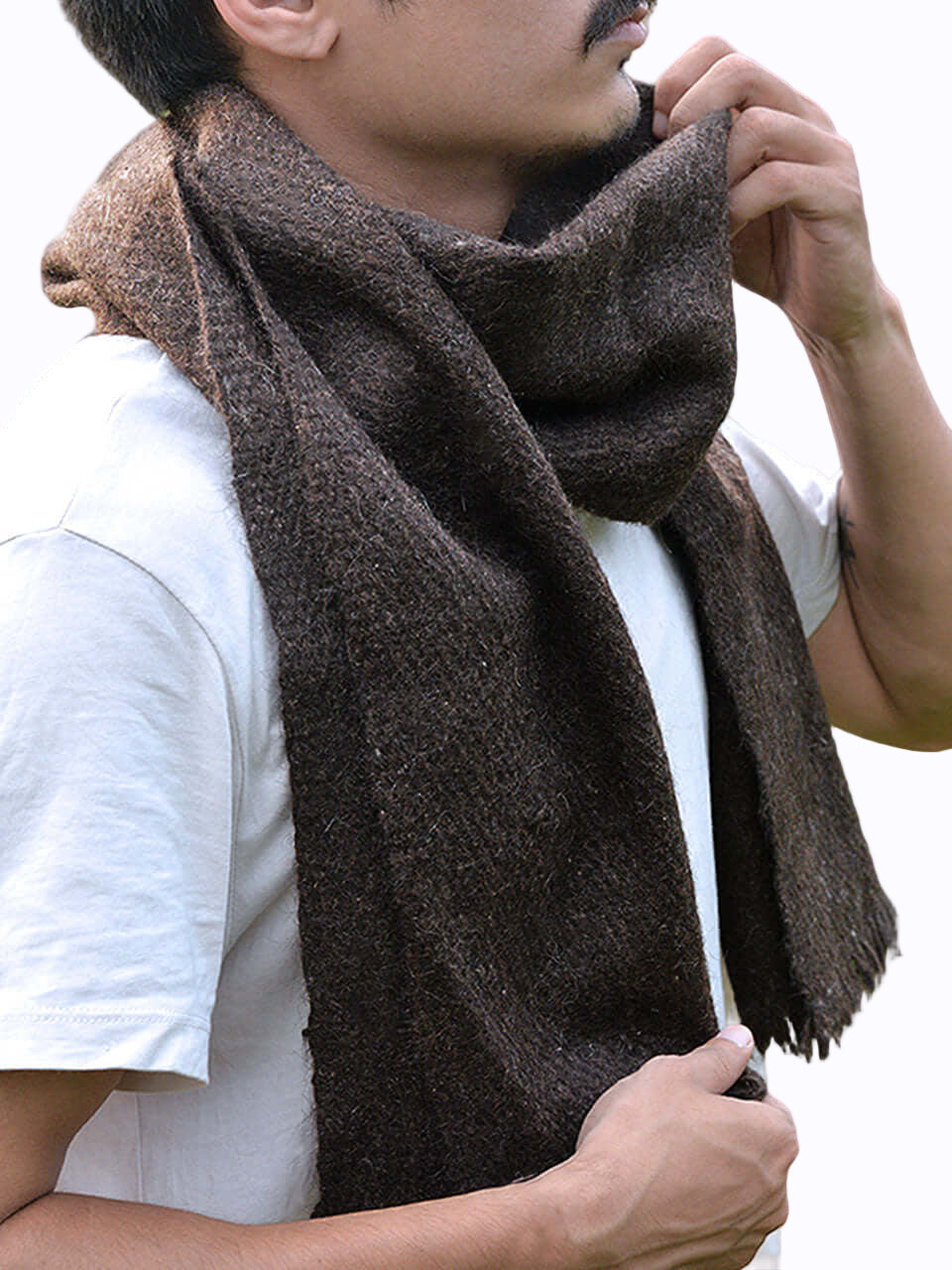 A man wearing a scarf stands in a lush green field, surrounded by nature and open skies
