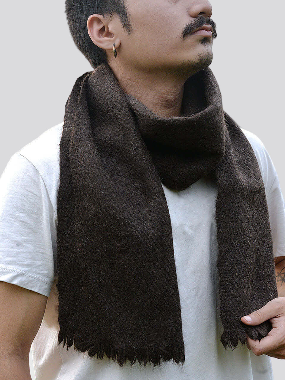 A man wearing a scarf stands in a lush green field, surrounded by nature and open skies