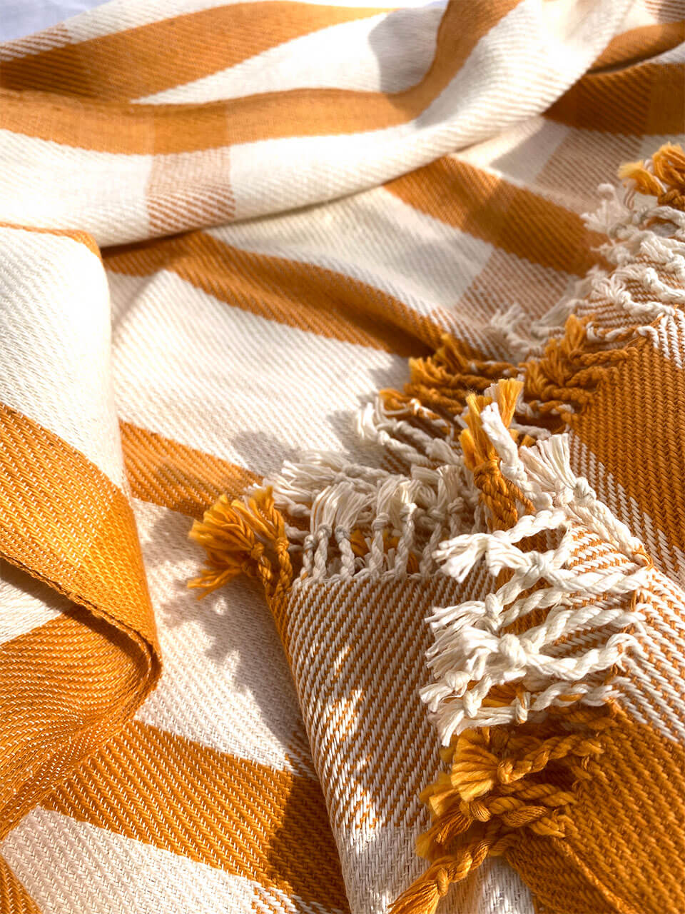 A yellow and white striped organic cotton bath towel with fringes, showcasing a vibrant and cozy design.