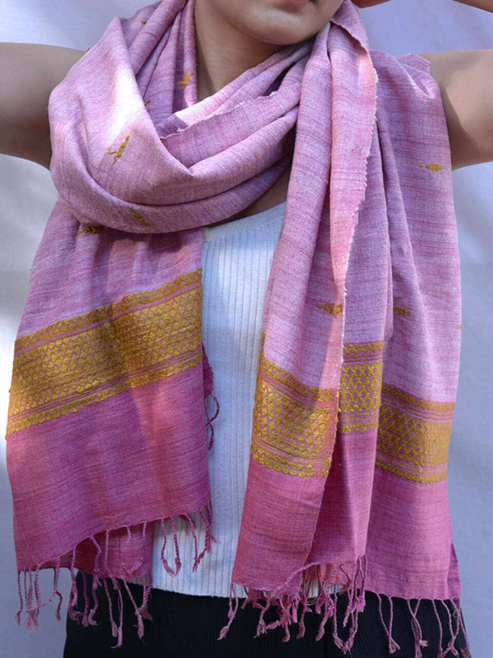 A woman elegantly draped in a pink scarf adorned with intricate gold embroidery.