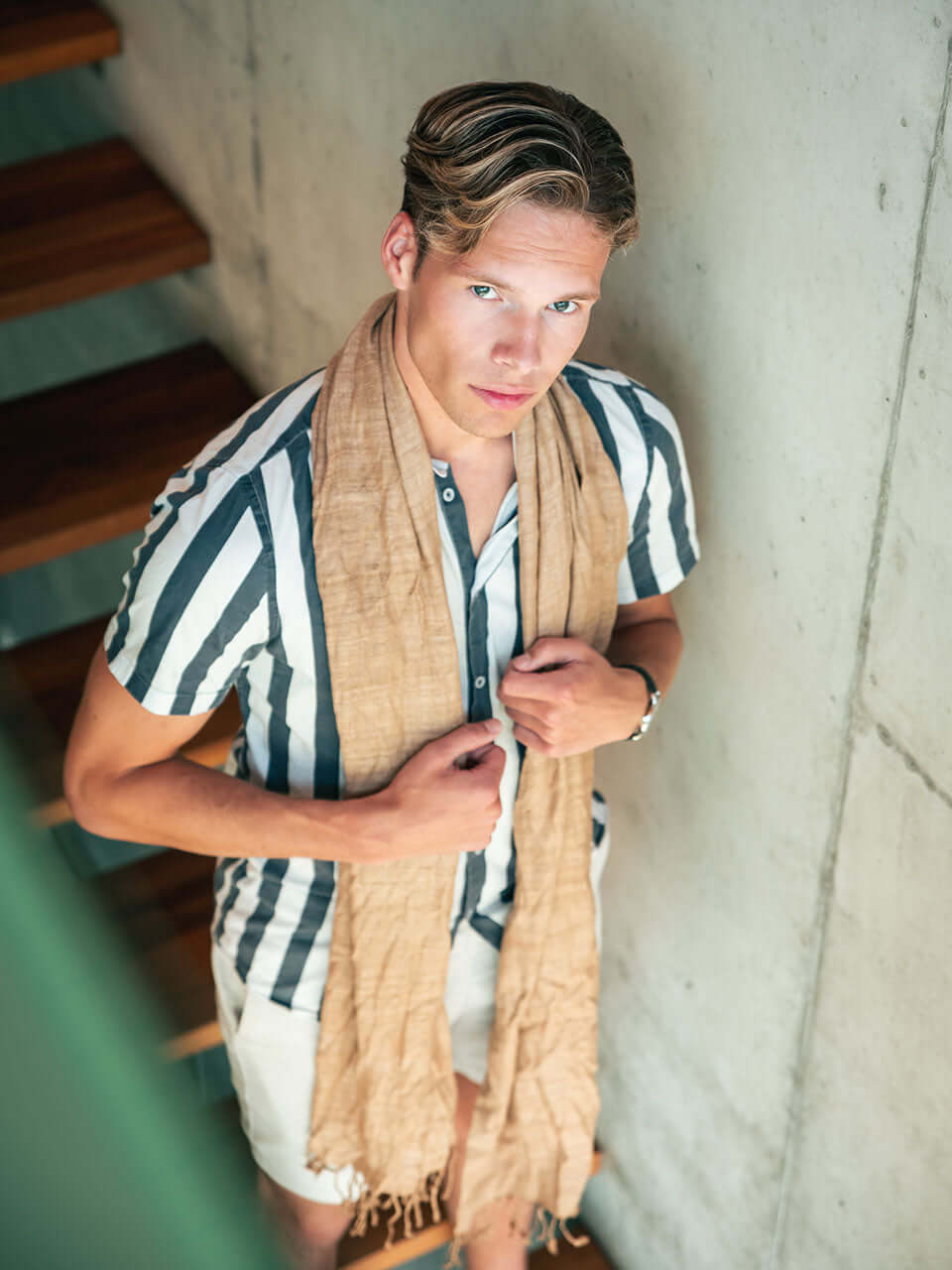 A man dressed in a striped shirt and a beige scarf, exuding a stylish and casual appearance.