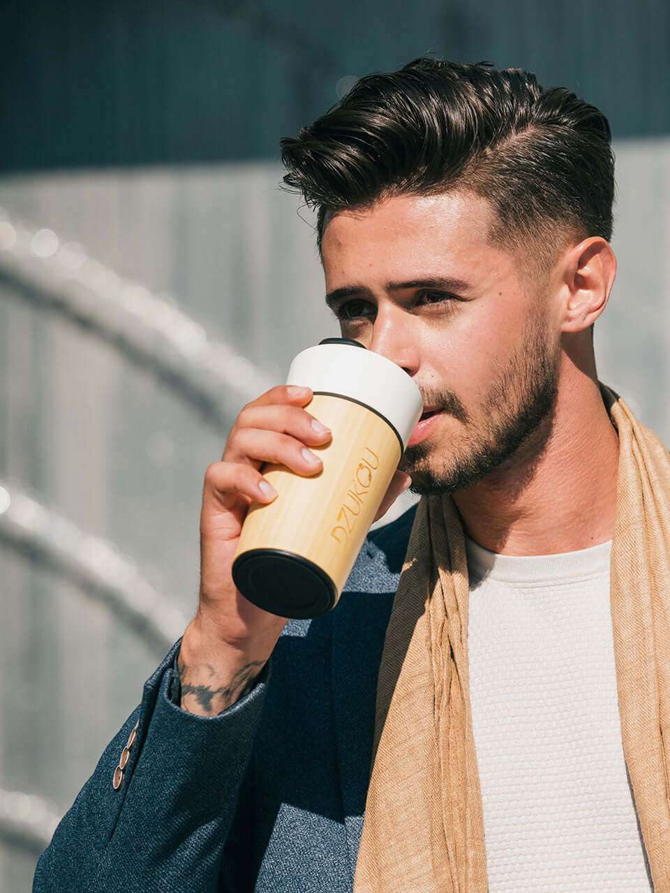 A man in a suit and a beige scarf enjoys a cup of coffee, exuding a sophisticated and relaxed demeanor.