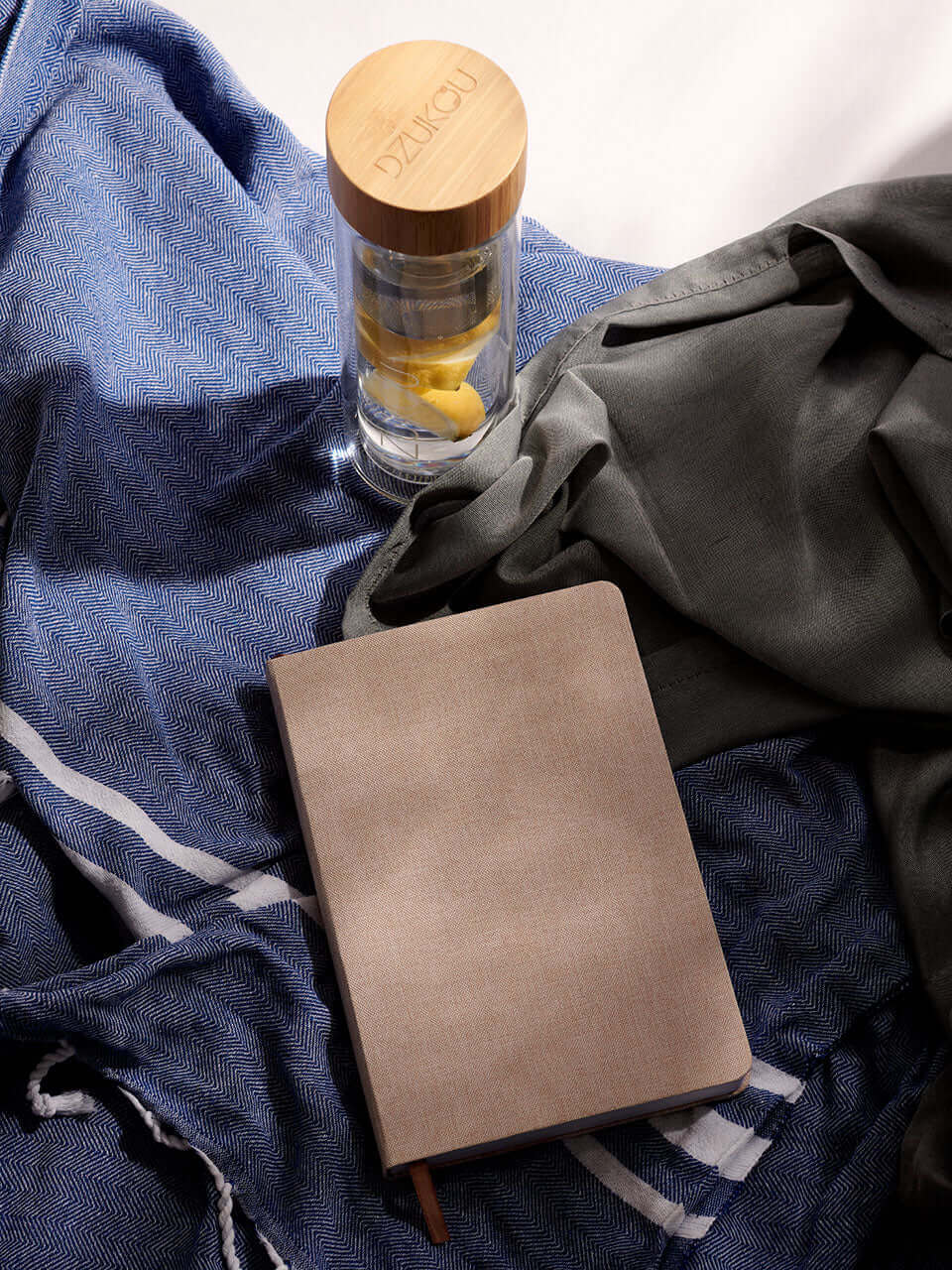 A linen notebook, a bottle of water, and a towel arranged neatly on a surface, suggesting a study or workout setting.
