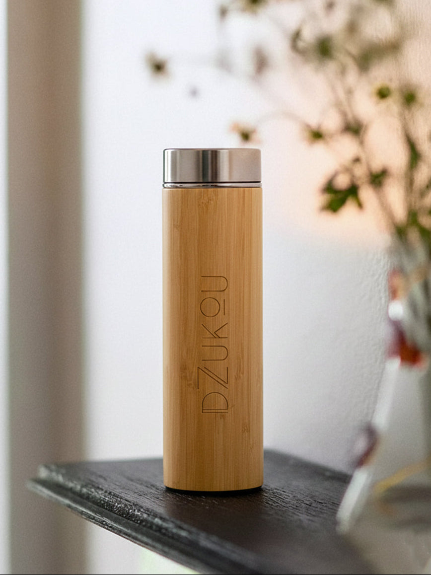Bamboo water bottle with silver cap on a surface with a blurred background