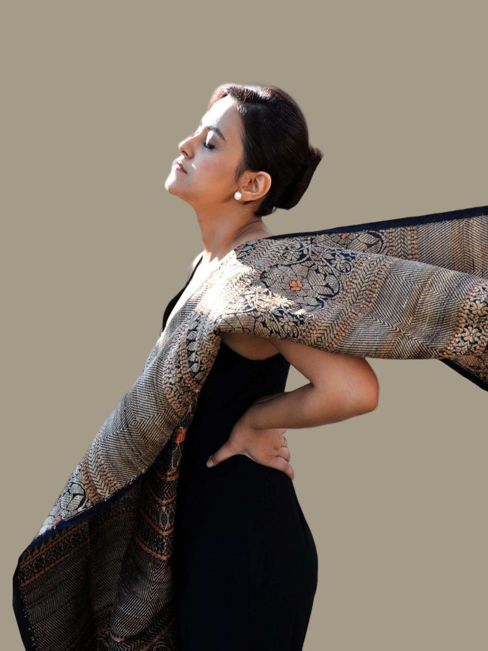 A woman in a black dress gracefully holds an ornate shawl, showcasing elegance and style.