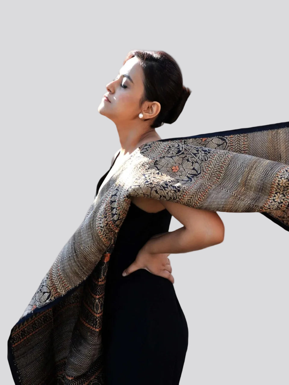 A woman in a black dress gracefully holds an ornate shawl, showcasing elegance and style.