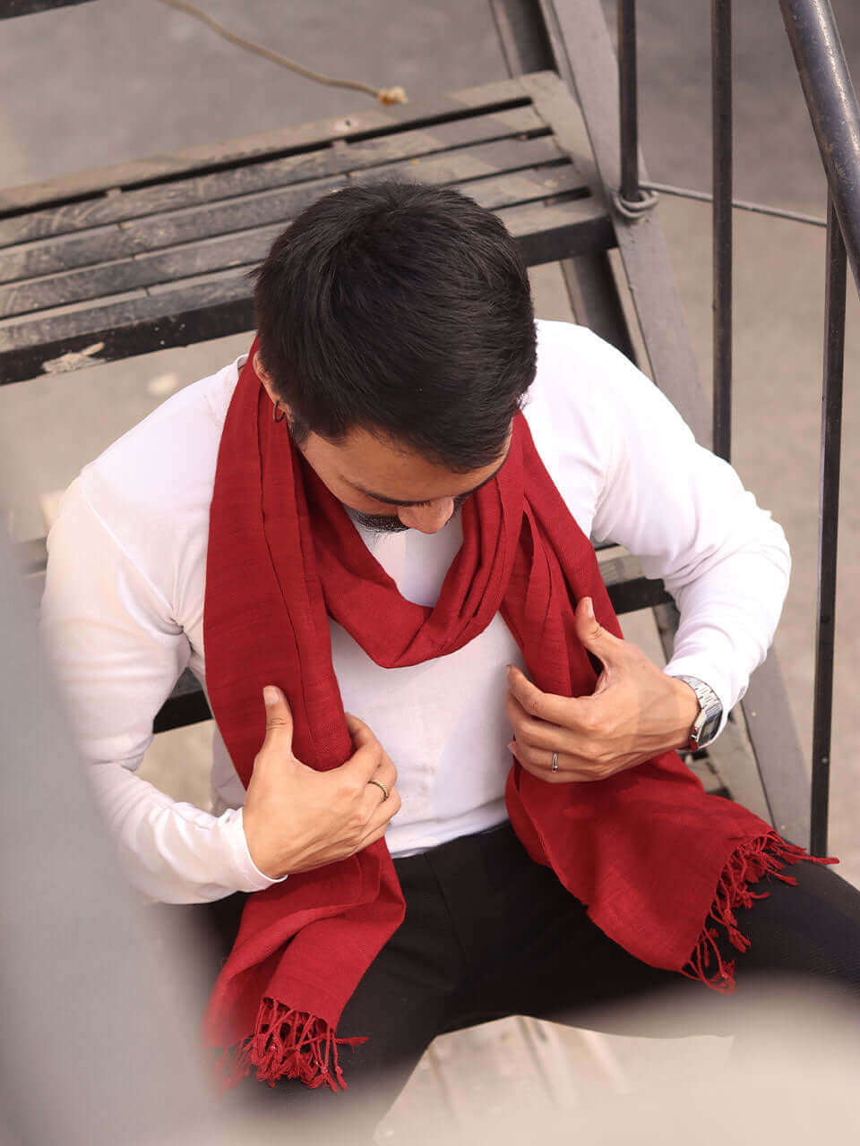 A man in a red scarf is seated on a bench, enjoying a moment of relaxation outdoors.