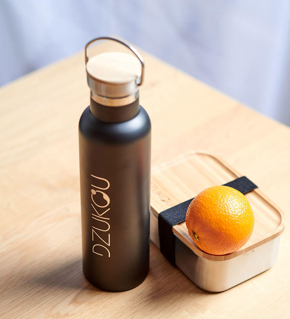 an orange kept with a lunchbox and a bottle
