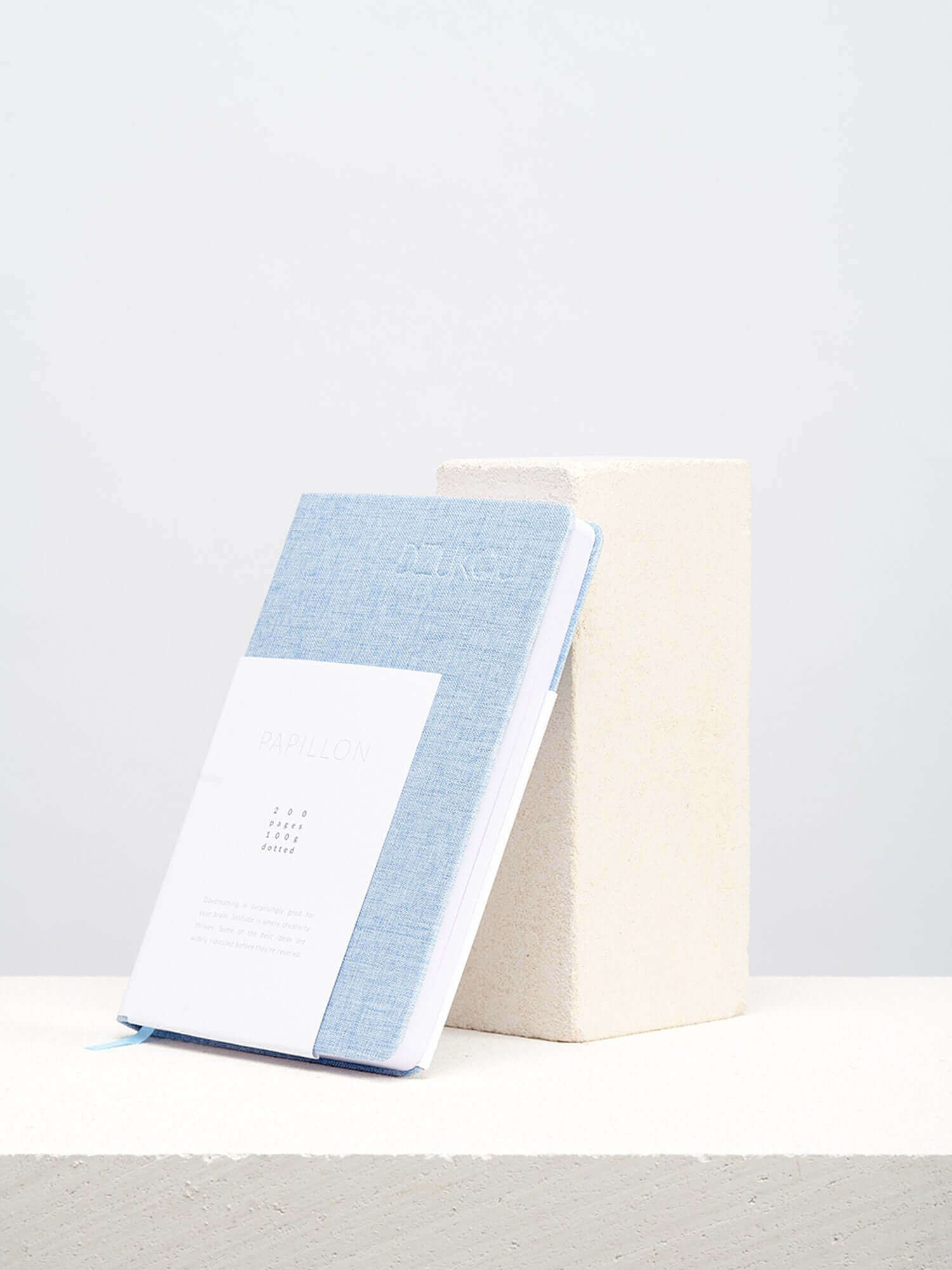A linen notebook place beside a white block with a clean white background.