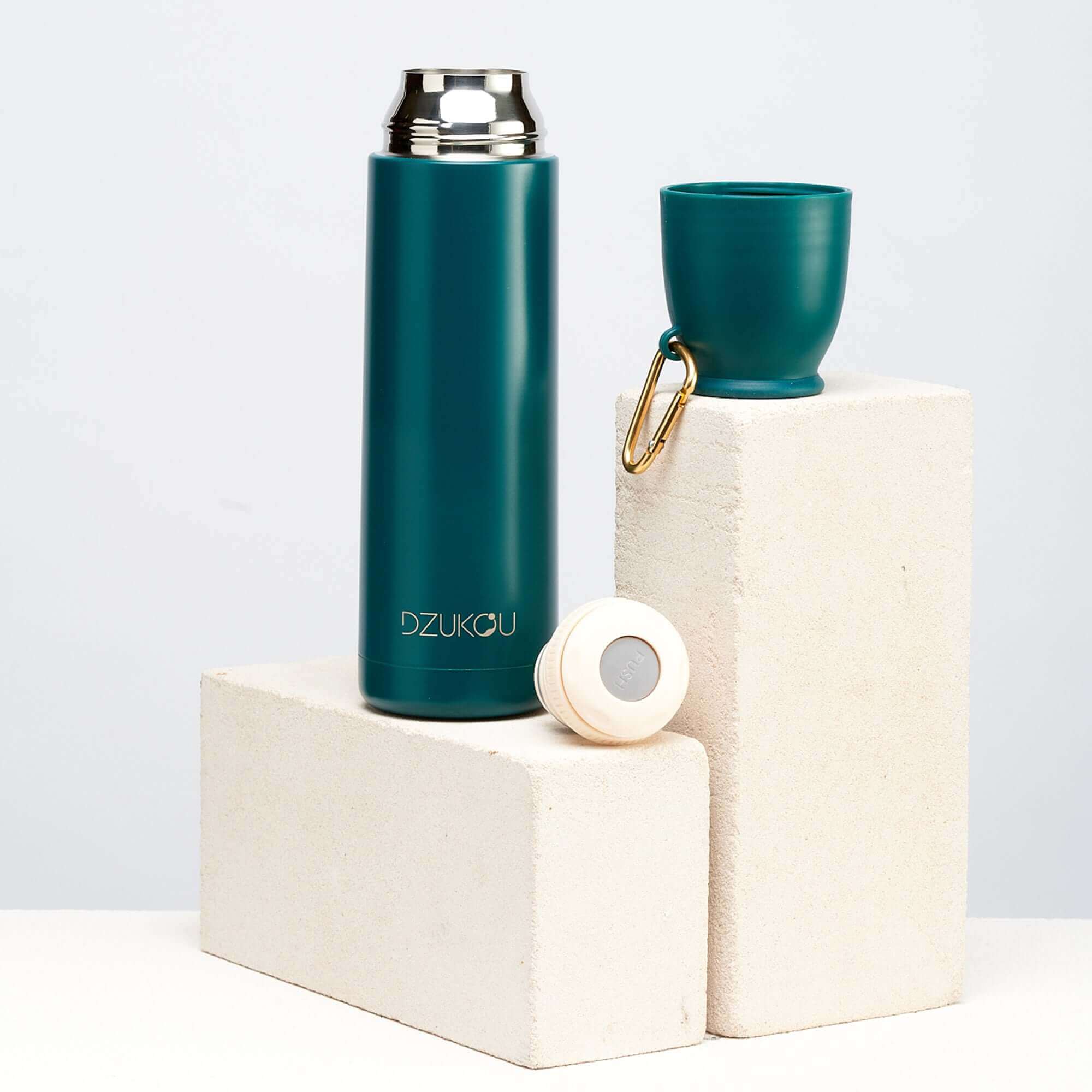A teal thermos flask and cup placed on a white block, showcasing a stylish and functional design.