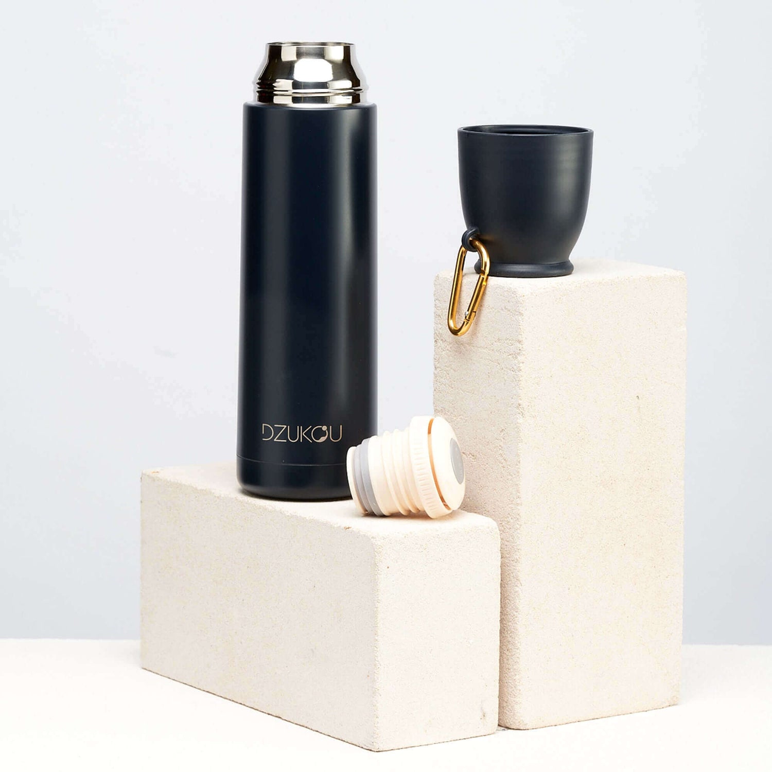 A black thermos flask and cup placed on a white block, showcasing a stylish and functional design.