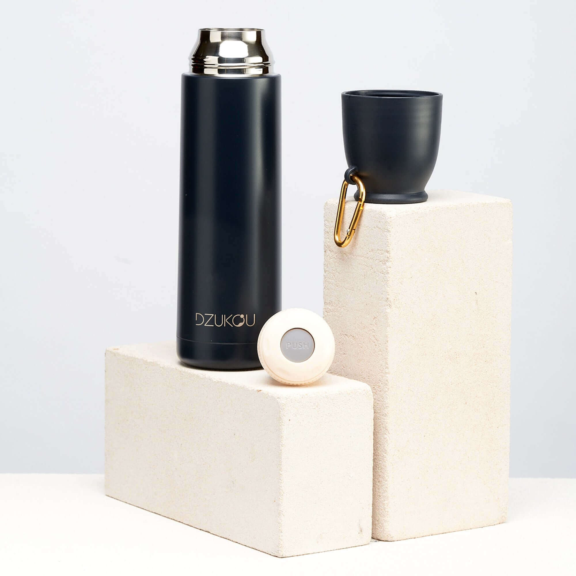 A black thermos flask and cup placed on a white block, showcasing a stylish and functional design.