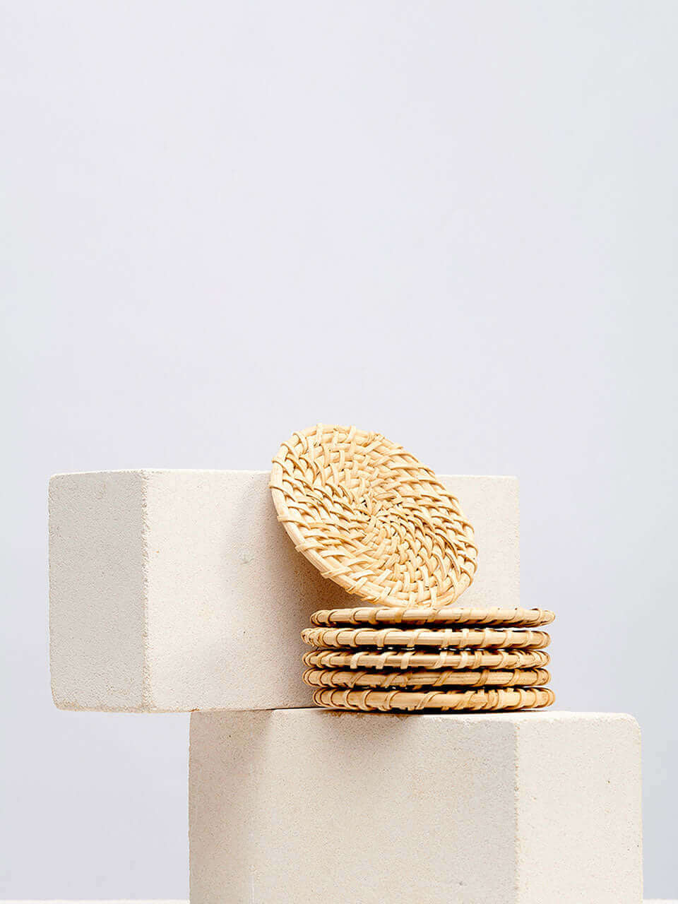 A stack of cane coasters in top of a white block, showcasing a simple yet elegant arrangement.
