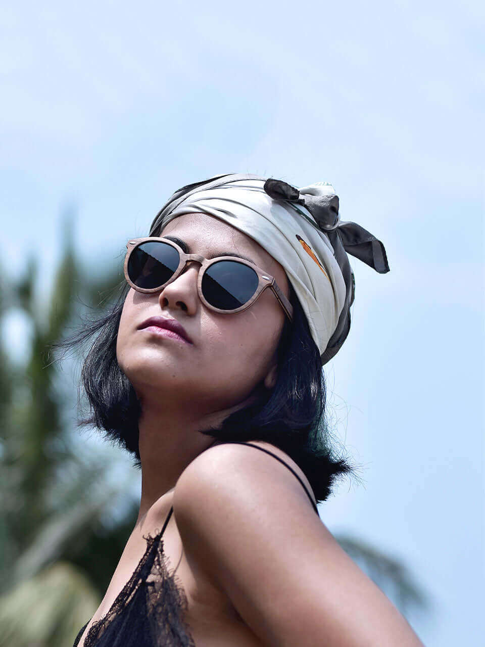 A woman with a wooden sunglasses and a head scarf, exuding elegance and style in a sunny outdoor setting.