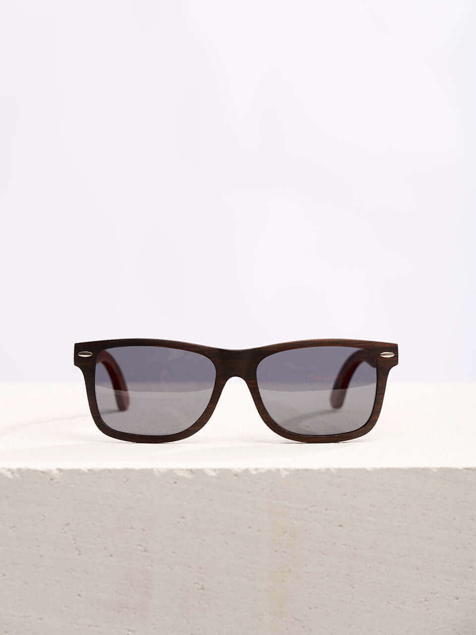 Wooden sunglasses with dark lenses in a neutral background, showcasing a unique and eco-friendly design. Perfect for stylish sun protection.