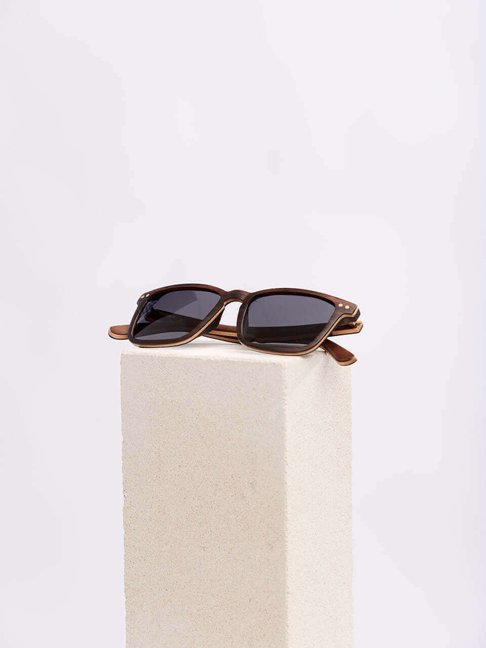 A pair of sunglasses resting on a wooden block, showcasing their sleek design against a natural background.
