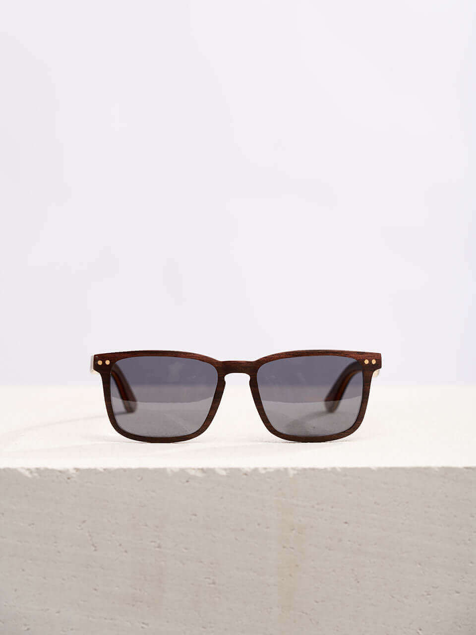 Wooden sunglasses with dark lenses in a neutral background, showcasing a unique and eco-friendly design. Perfect for stylish sun protection.