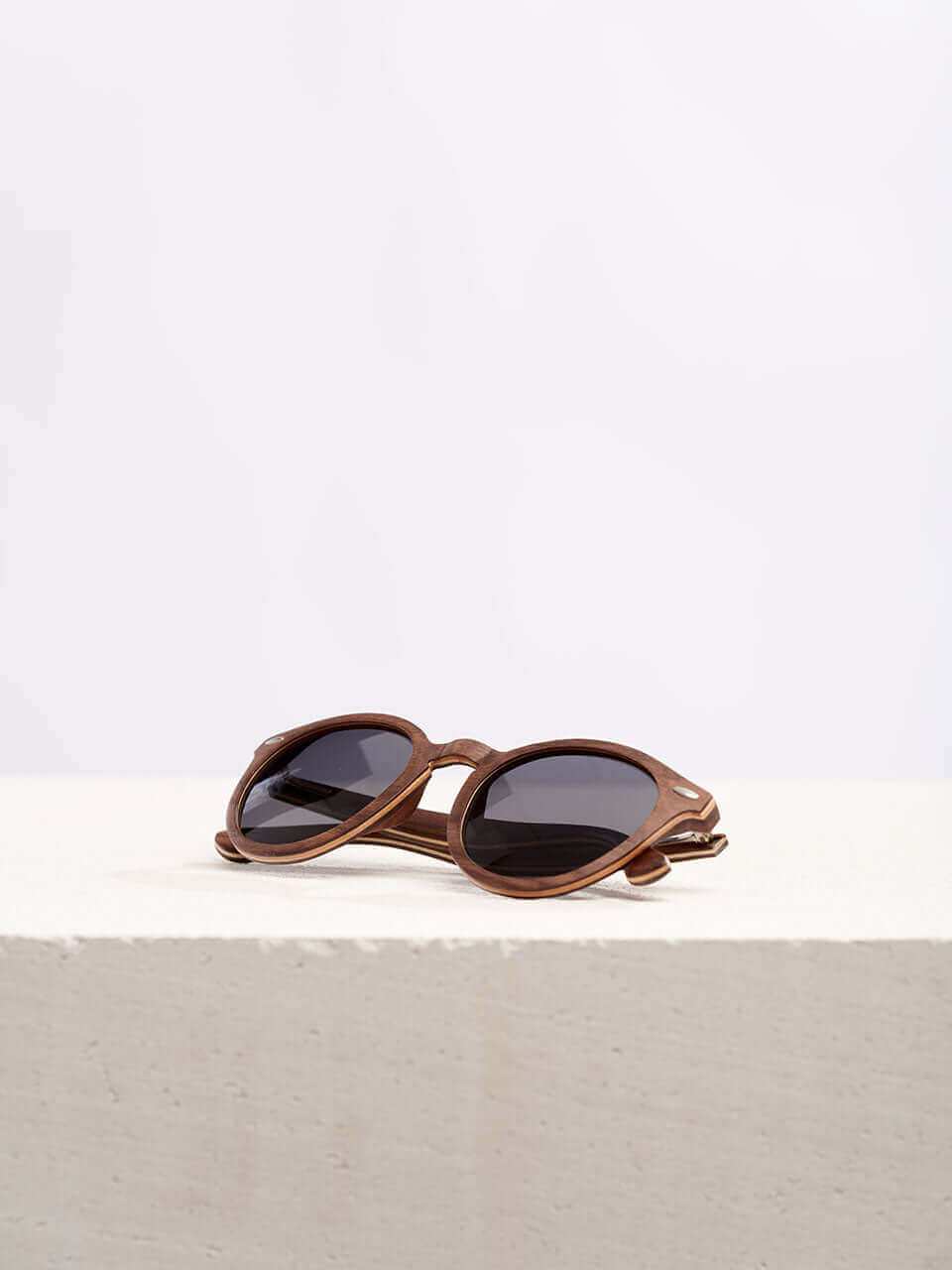 A pair of stylish wooden sunglasses resting on a clean white surface, showcasing their sleek design and reflective lenses.