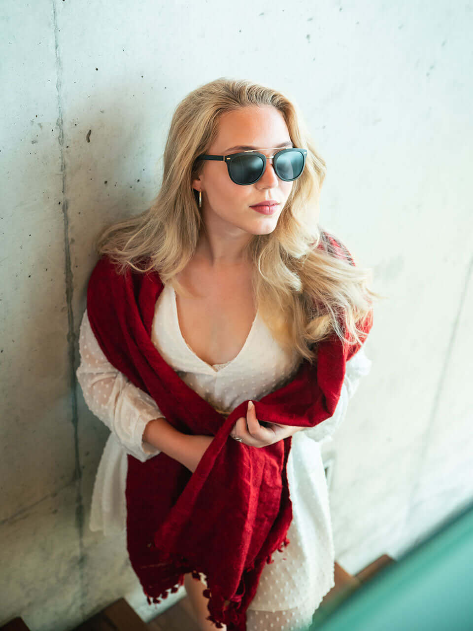 A woman wearing a wooden sunglass and a red scarf, exuding confidence and style in a bright outdoor setting.