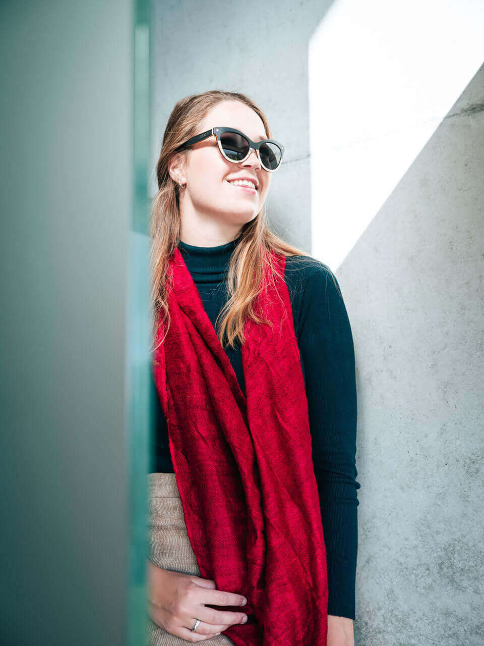 A woman with cat eye sunglass and a red scarf, exuding confidence and style in a sunny outdoor setting.