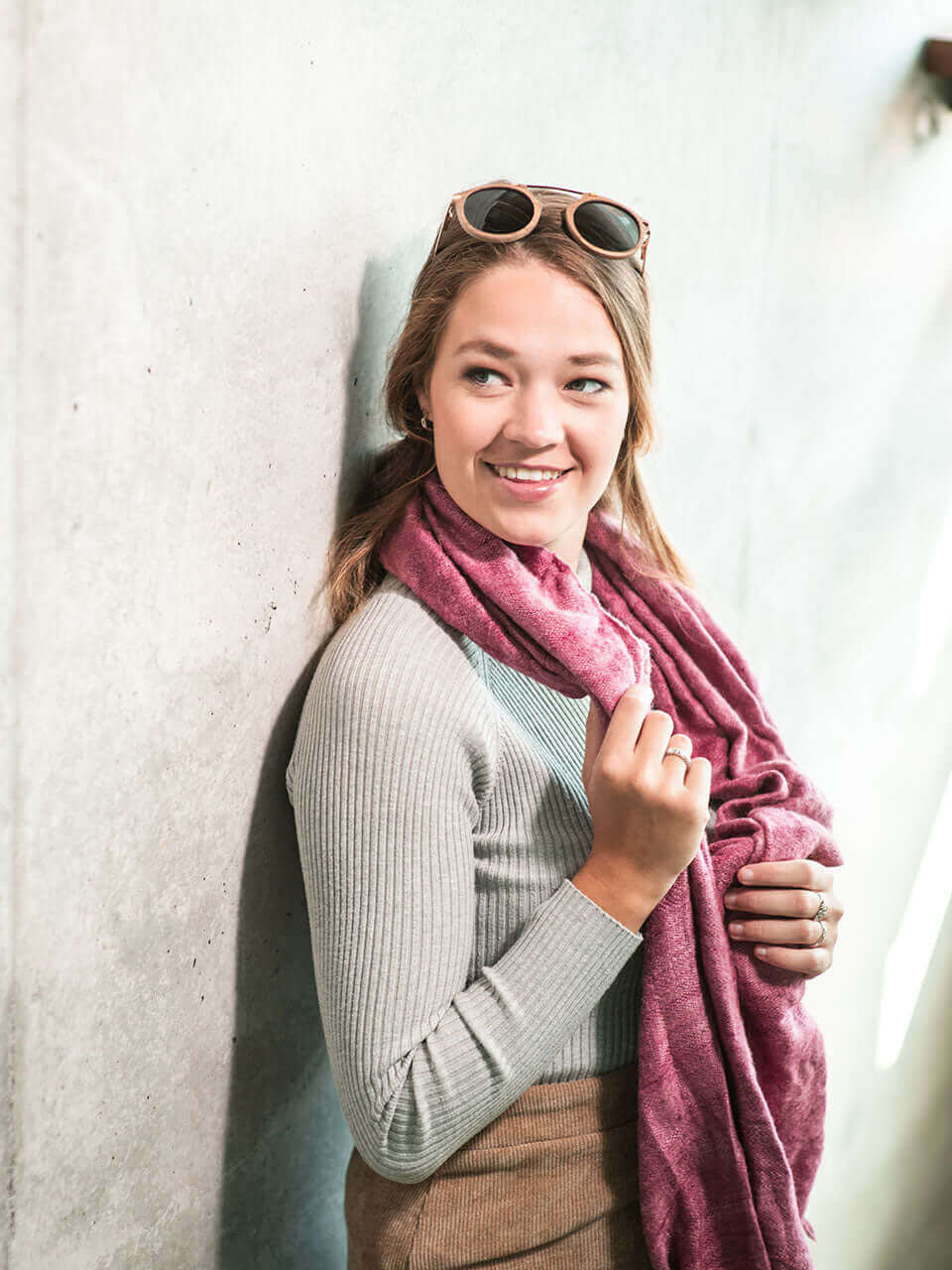A woman with wooden sunglasses and a pink scarf, exuding a stylish and confident demeanor.