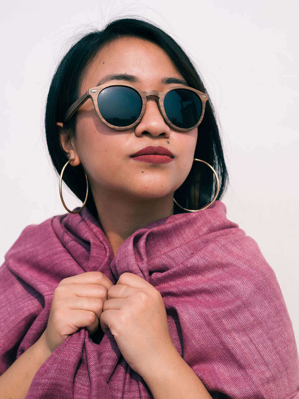 A woman with sunglasses and a pink scarf, exuding elegance and style in a sunny outdoor setting.