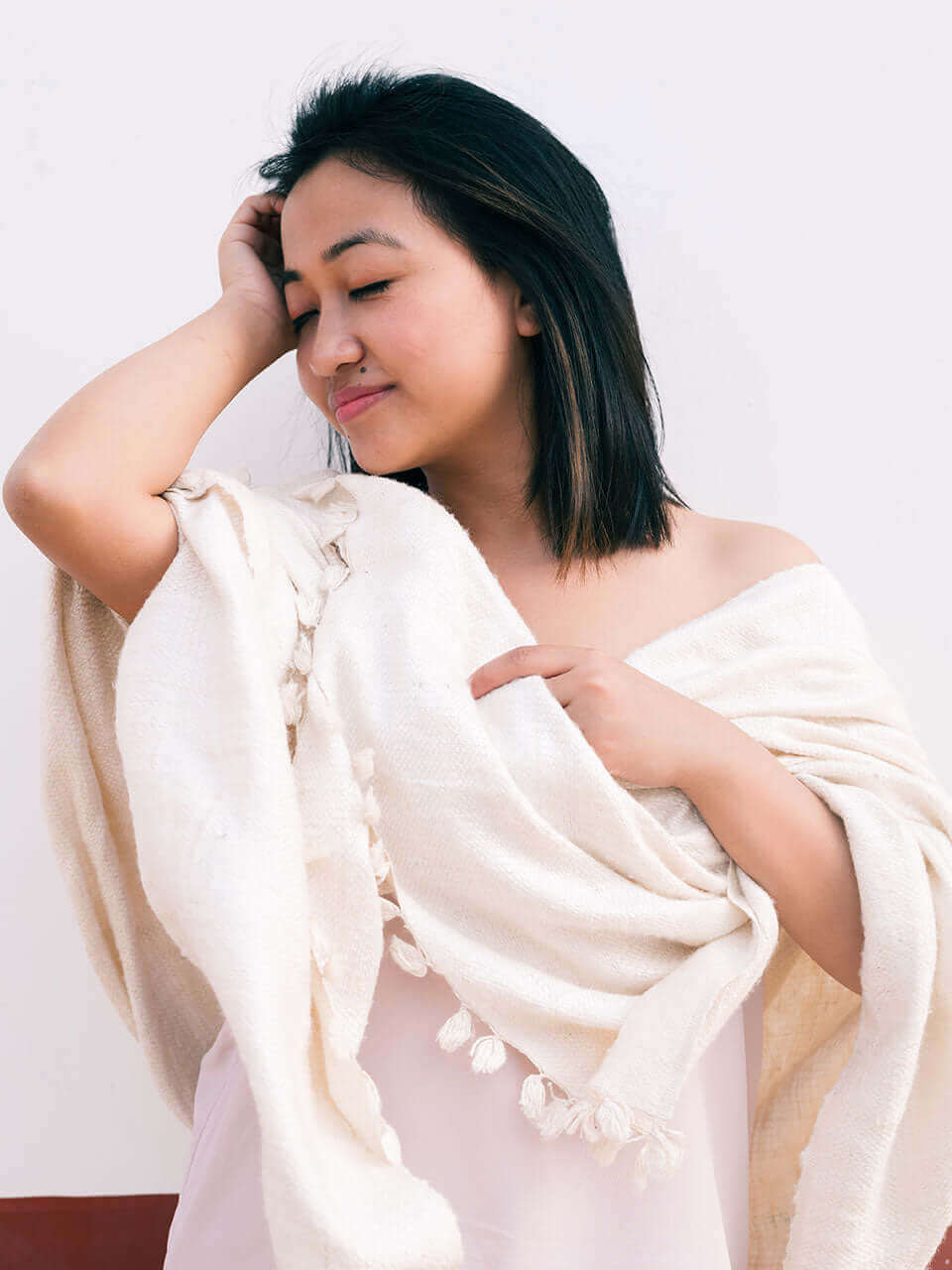 A woman draped in a soft, elegant white Eri silk shawl, showcasing its smooth texture and natural color.
