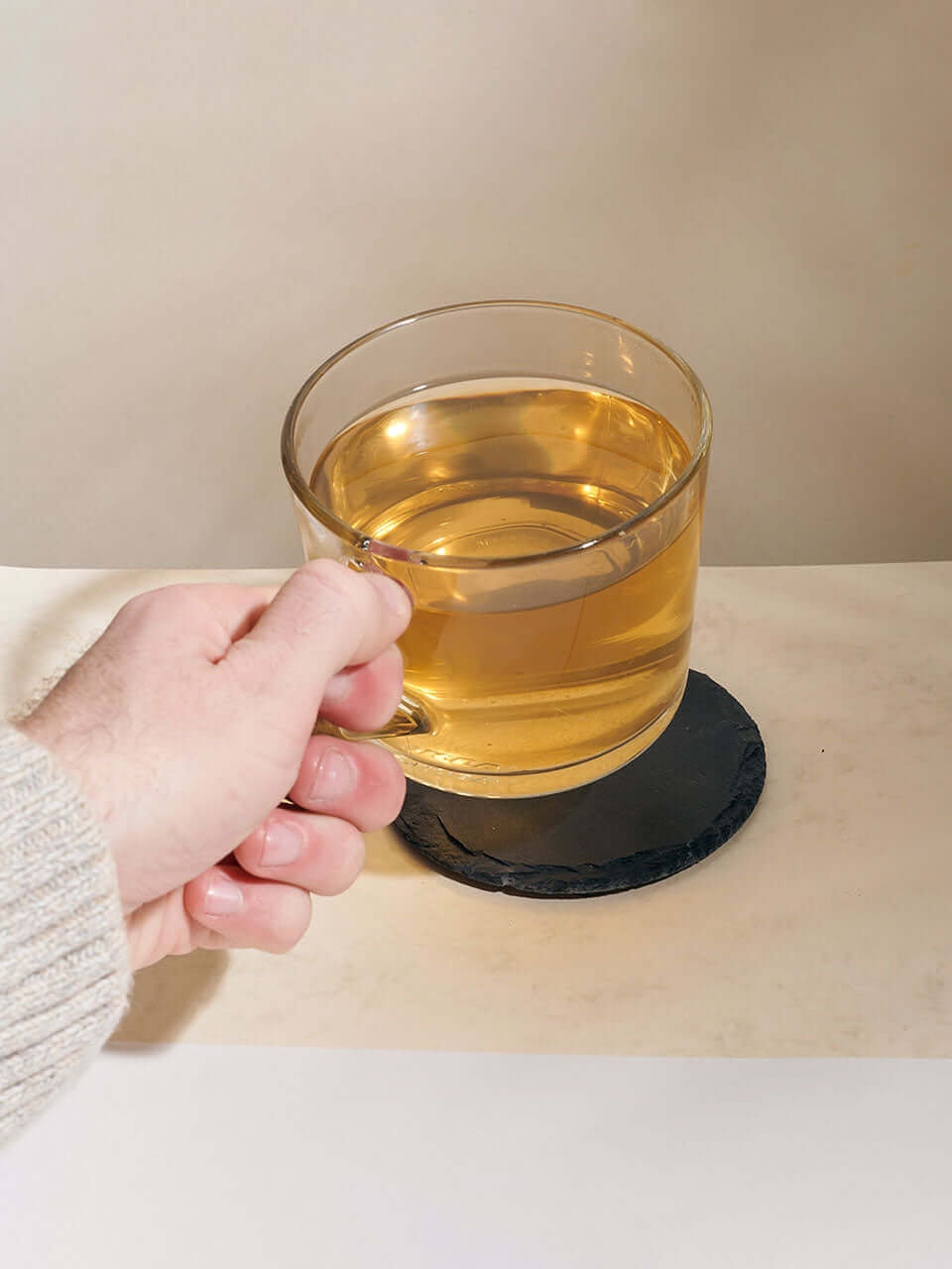A person holding a cup of tea, resting it on a slate coaster, with a serene background.