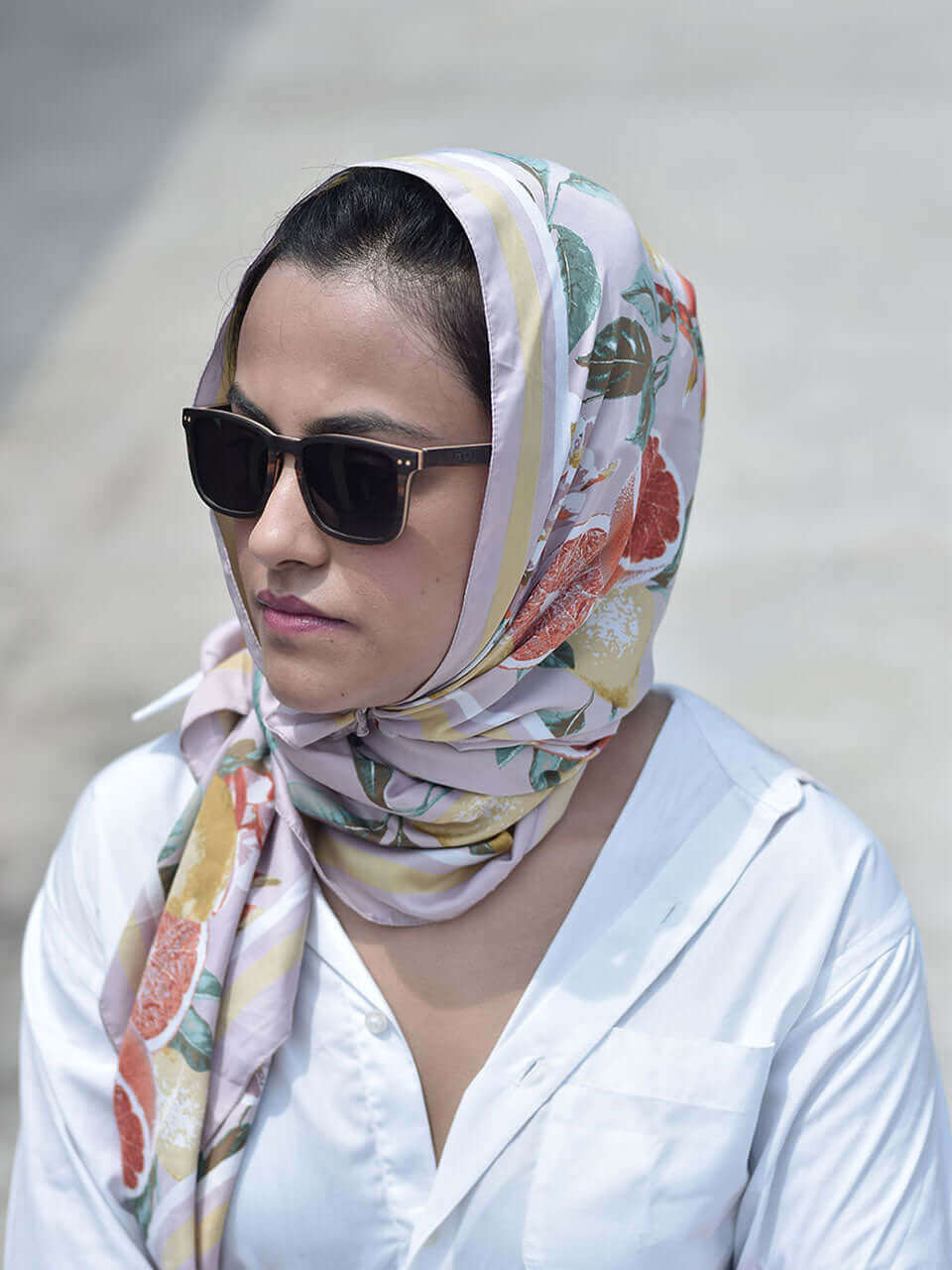 A woman with sunglasses and a floral scarf, exuding elegance and style in a bright outdoor setting.