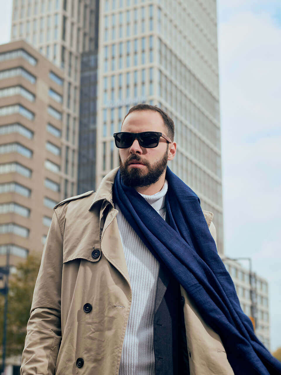 A man wearing a trench coat and a wooden sunglasses stands confidently, exuding an air of mystery and sophistication.