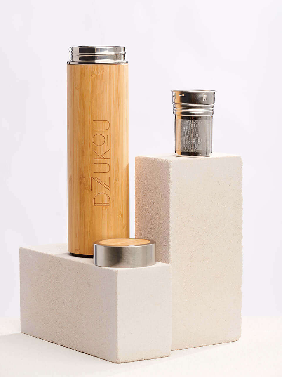 A bamboo water bottle with a lid and a infuser sits atop a white block, showcasing a simple yet elegant storage solution.