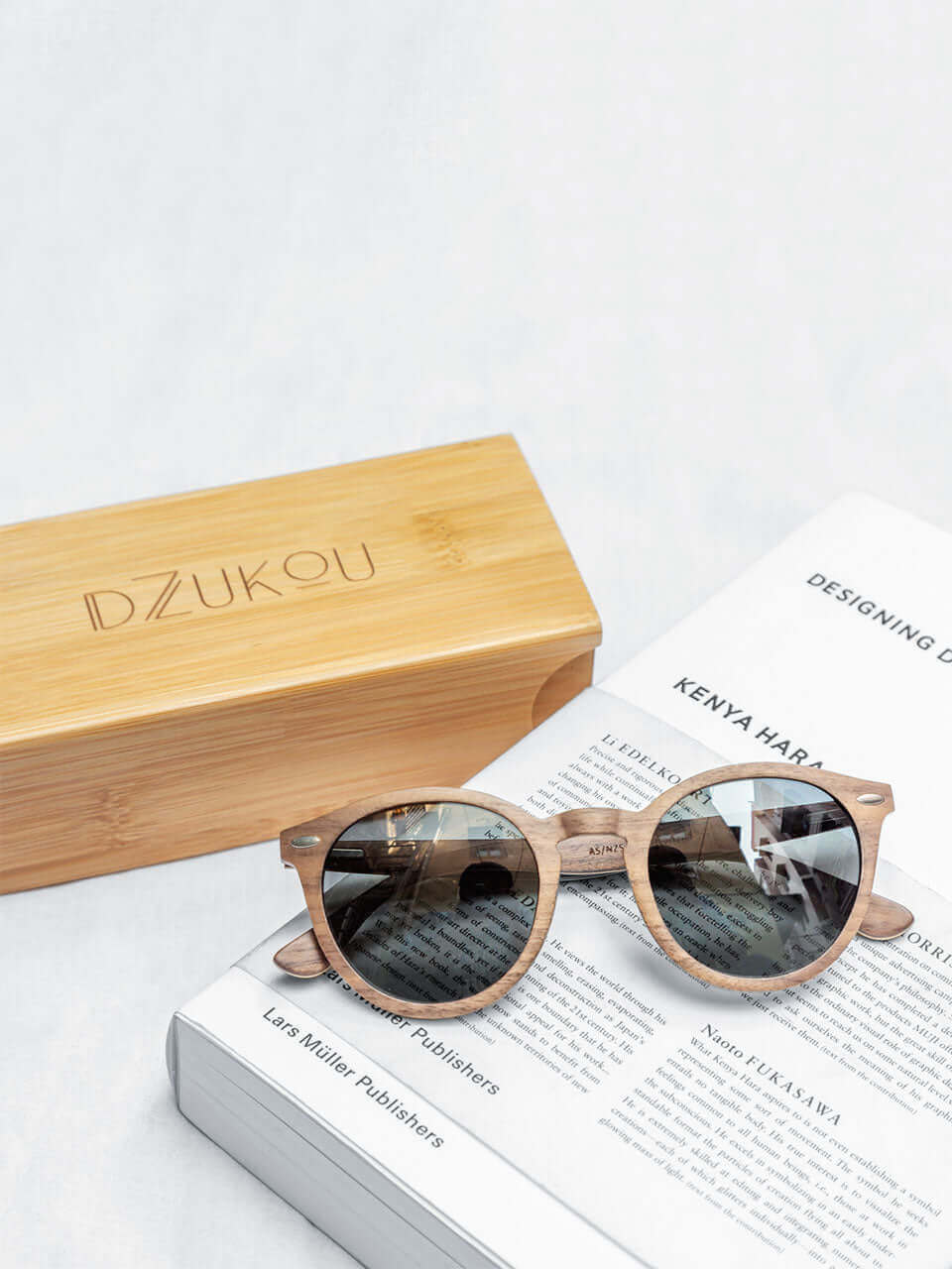 Wooden sunglasses resting on an open book beside a wooden box, showcasing a blend of nature and literature.