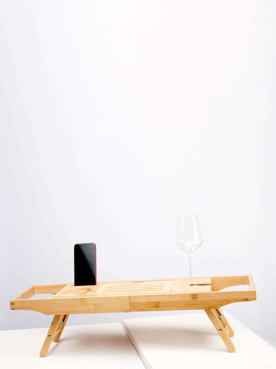 A wooden bath tub caddy featuring a bench design with two legs and a wooden tray for holding items.