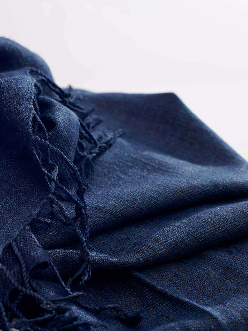 A dark blue scarf with fringes elegantly draped, showcasing its rich color and texture.