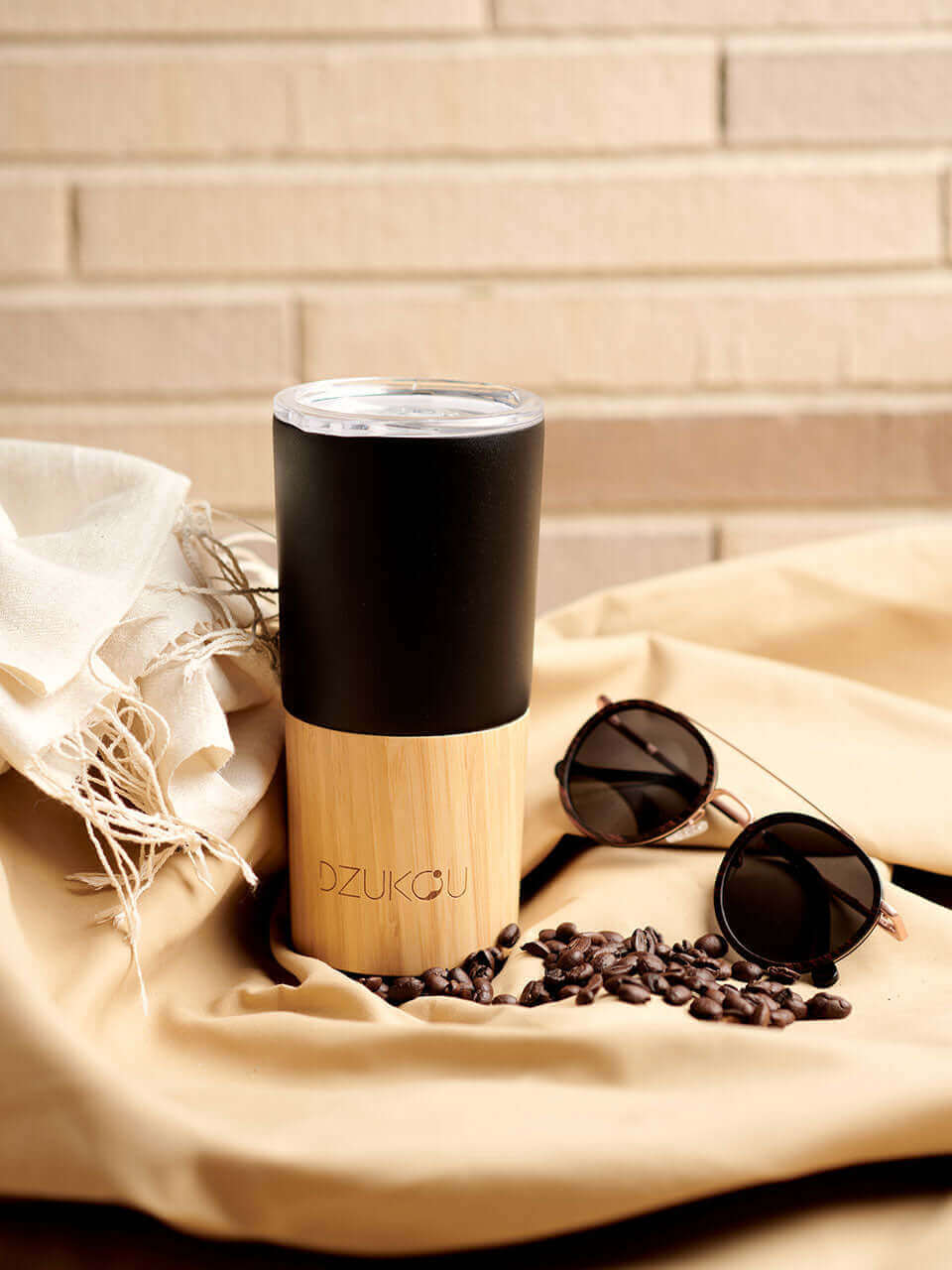 A black and white bamboo coffee tumbler with a sunglass on the side, surrounded by scattered coffee beans.