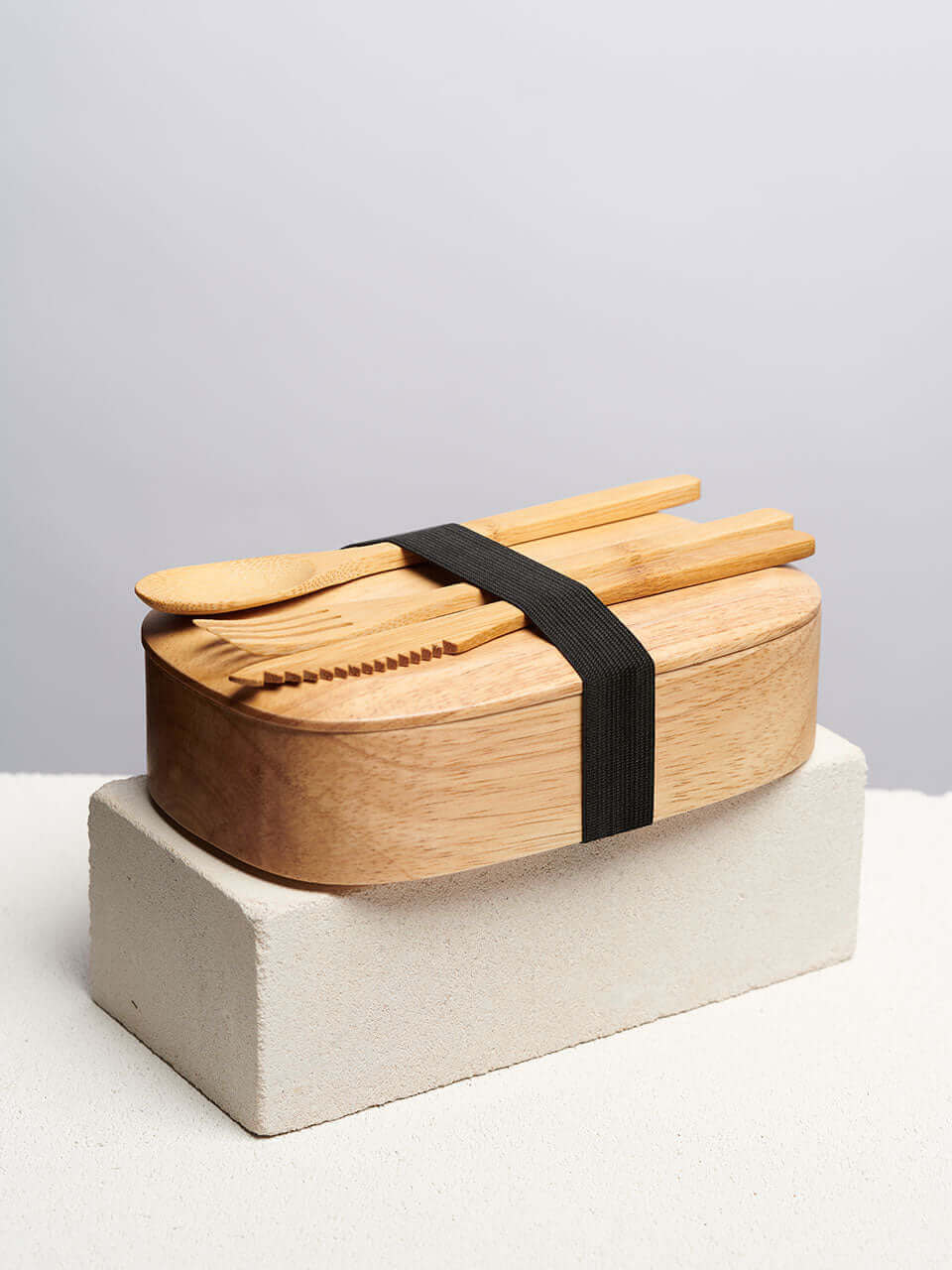 A wooden lunch box with two wooden utensils resting on its surface, showcasing a natural and rustic aesthetic.
