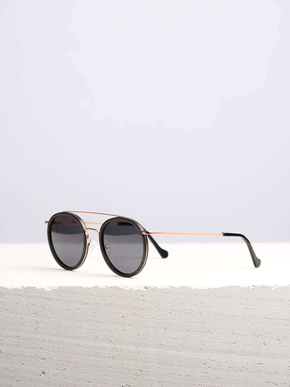 A wooden sunglasses featuring a stylish sleek black frame complemented by elegant gold rims in a clean surface with a neutral background, showcasing a unique and eco-friendly design.
