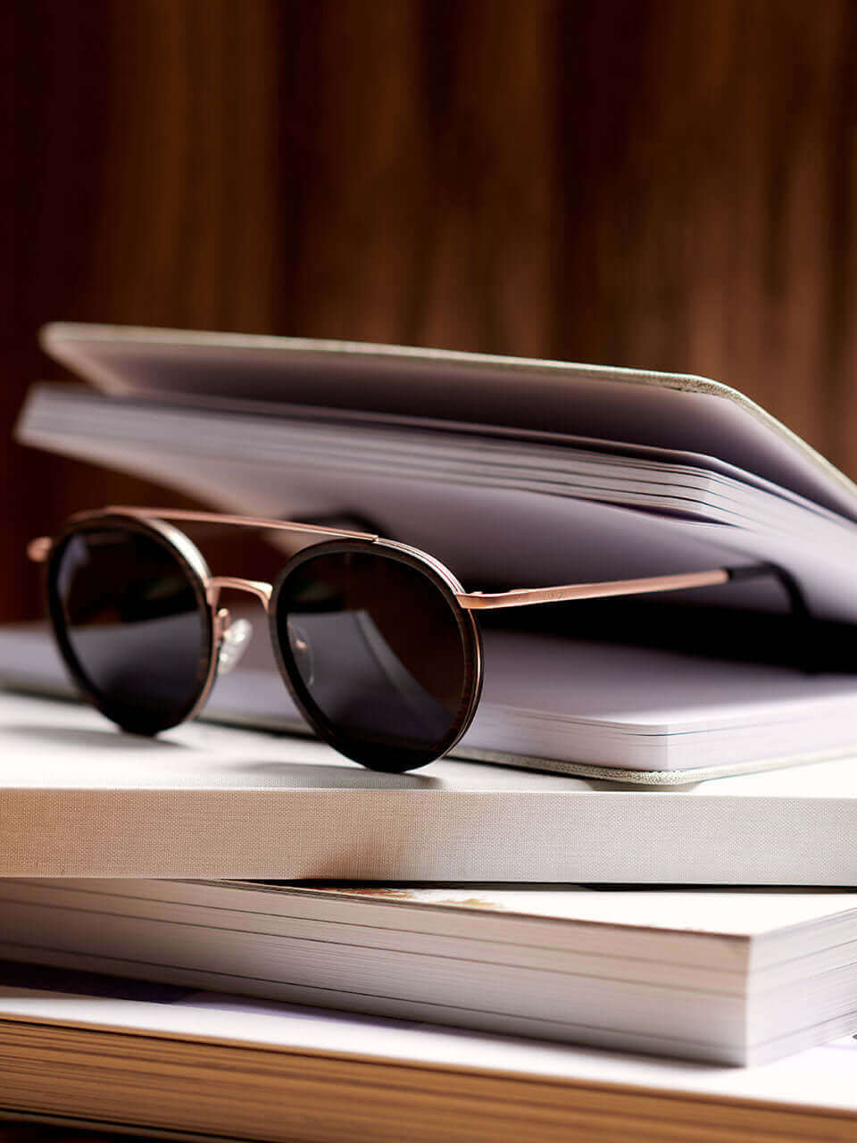 A wooden sunglass resting on a stack of a note book, symbolizing leisure and knowledge.