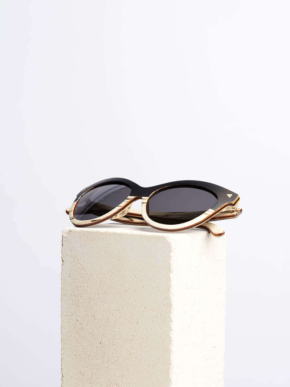A wooden cat eye sunglass resting on a solid block surface, showcasing their sleek design and reflective lenses.