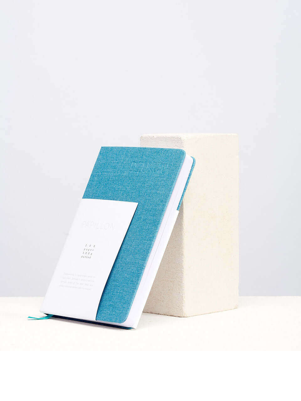 A linen notebook place beside a white block with a clean white background.