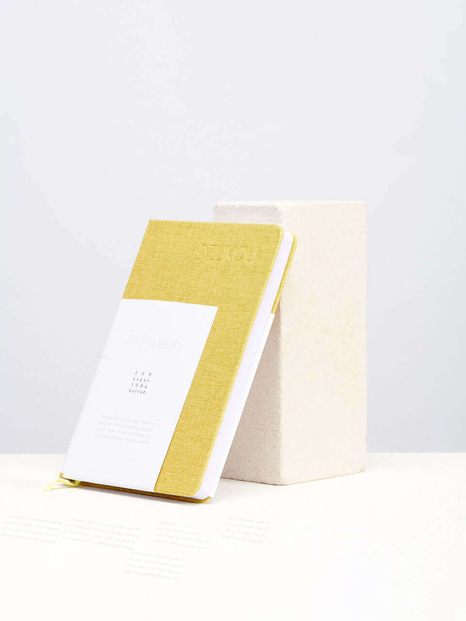 A linen notebook place beside a white block with a clean white background.